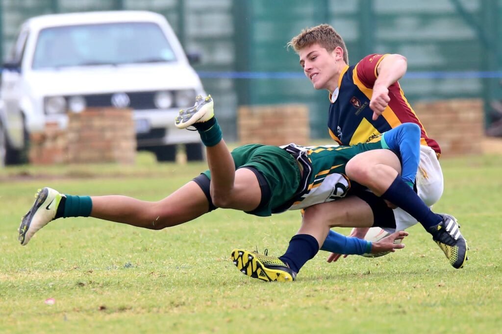 Two young athletes engaged in a dynamic rugby tackle during a competitive match.